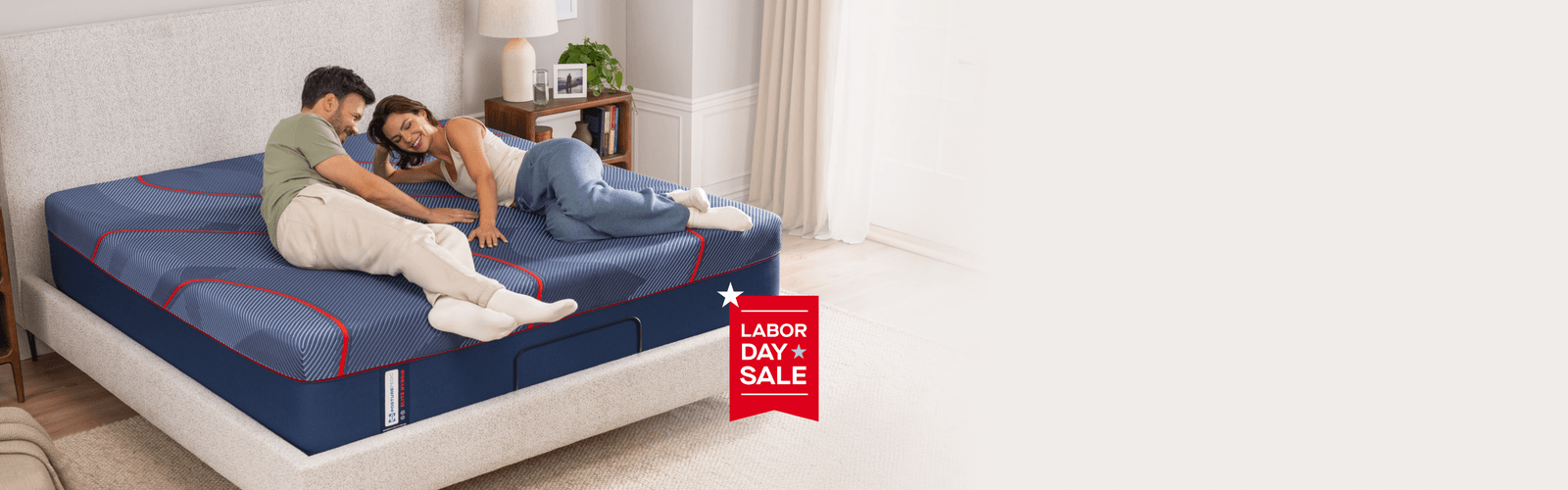 couple laying on an Elite mattress with an overlay banner that says, "Labor Day Sale"