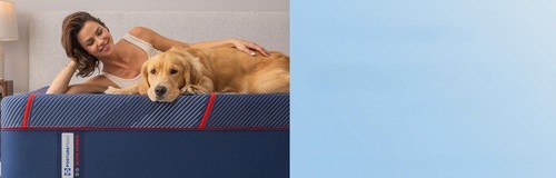 Smiling woman and golden retriever laying on posture-pedic elite hybrid mattress