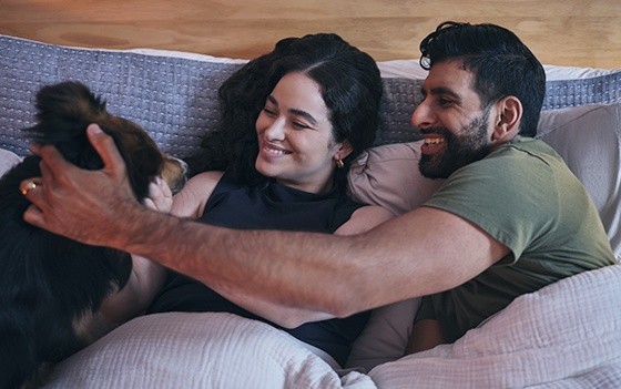 Couple laying with dog on mattress