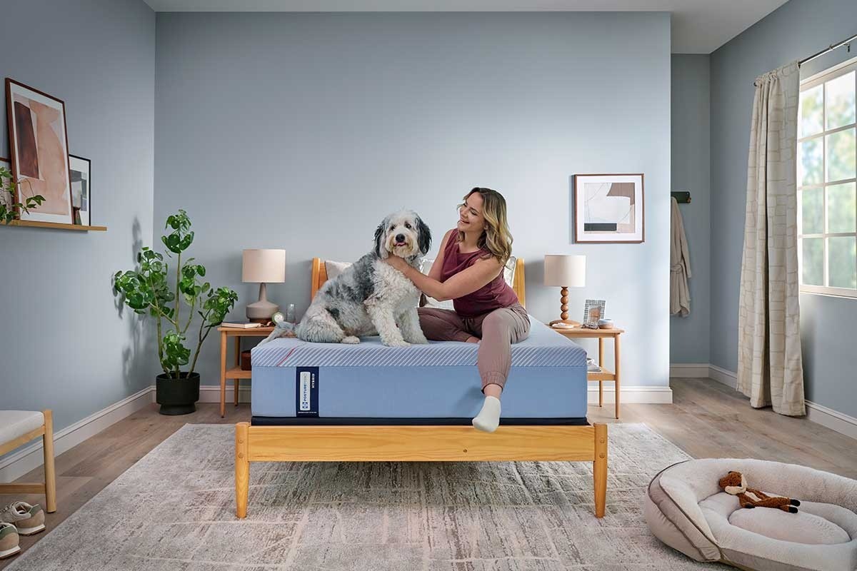 A woman petting a dog while sitting on a bed