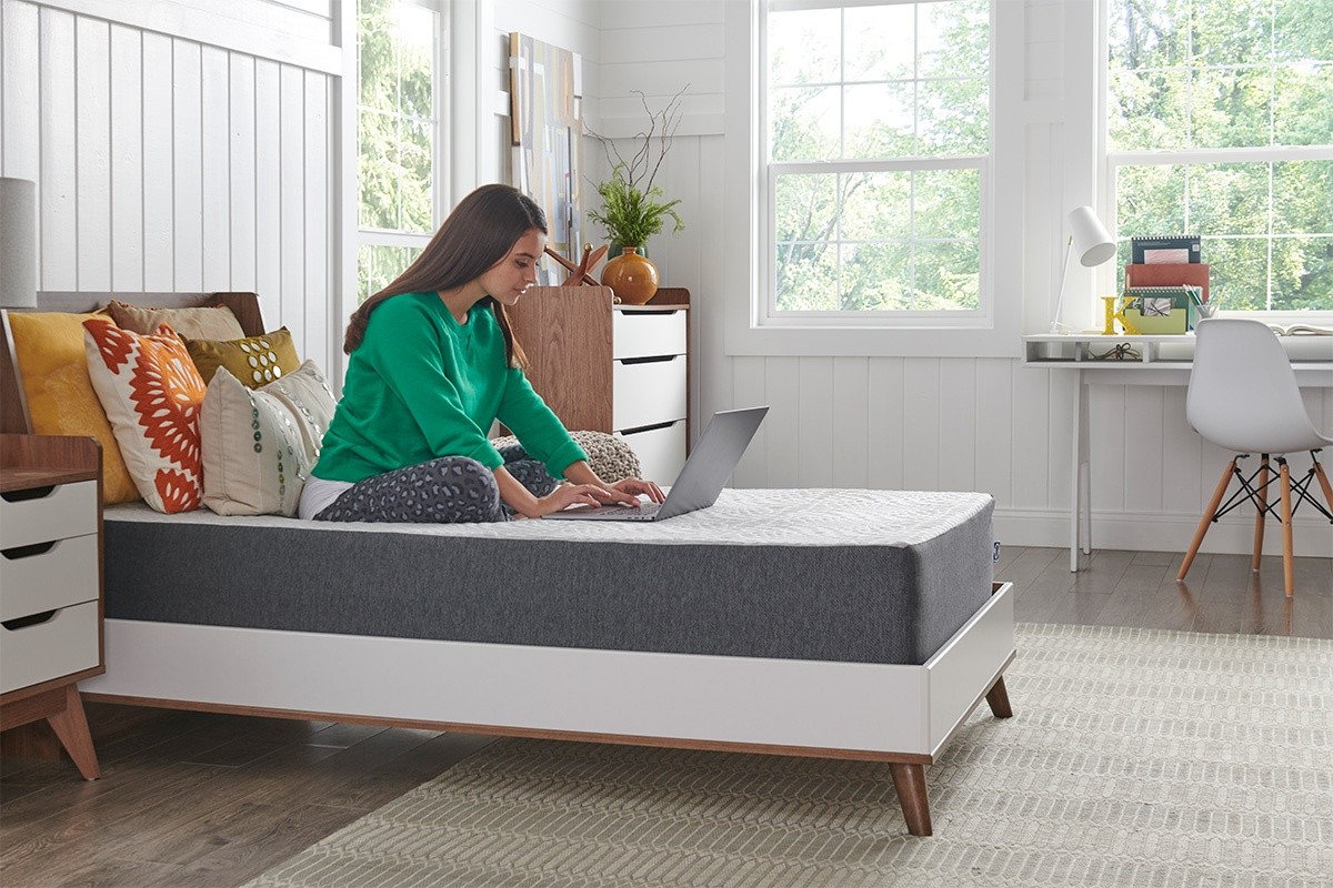 Woman sitting on a mattress while working on a laptop in a styled room