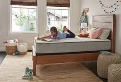 A young girl doing homework on a Sealy Essentials mattress.